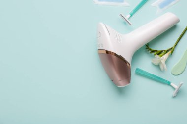 Usturalı modern fotoepilatör, balmumu şeritler ve turkuaz arka planda çiçek.