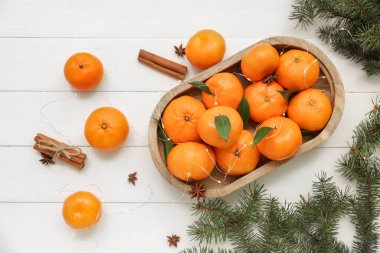 Noel ışıkları parlayan bir tepsi tatlı mandalina ve beyaz ahşap arka planda tarçın