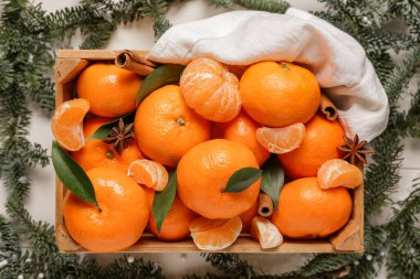 Tarçınlı bir kutu tatlı mandalina, yıldız anason ve beyaz ahşap arka planda köknar dalları.