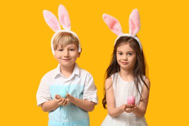 Sarı arka planda Paskalya yumurtaları olan tavşan kulaklı şirin çocuklar.