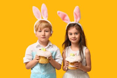 Sarı arka planda Paskalya pastaları olan tavşan kulaklı şirin çocuklar.