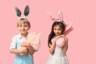Pembe arka planda Paskalya hediyesi yumurtaları olan tavşan kulaklı şirin çocuklar.