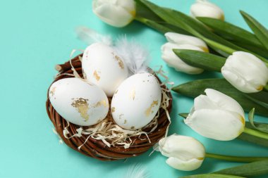 Paskalya yumurtalı yuva, turkuaz arka planda tüyler ve laleler