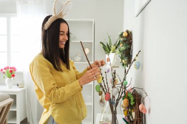 Tavşan kulaklı, söğüt dallarını evde paskalya yumurtasıyla süsleyen genç bir kadın.