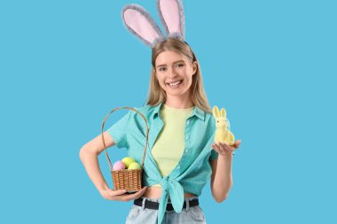 Tavşan kulaklı genç bir kadın. Mavi arka planda Paskalya tavşanı ve yumurtaları var.