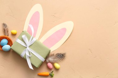 Hediye kutulu Paskalya yumurtaları, tüyler ve bej arka planda kağıt tavşan kulakları.