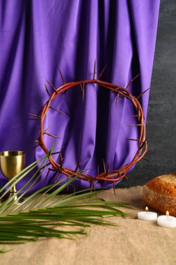 Dikenli taç, ekmek, kadeh ve mor kumaş arka planda palmiye yaprağı.