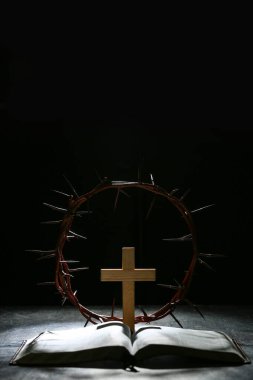 Ahşap haçlı dikenli taç, siyah grunge arka planda İncil ve ışık