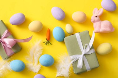 Tüylü boyanmış Paskalya yumurtaları ve sarı arka planda hediye kutuları.