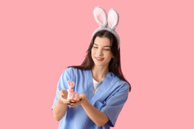 Pembe arka planda Paskalya tavşanı olan tavşan kulaklı kadın doktor.