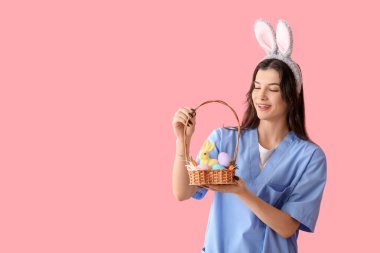 Pembe arka planda Paskalya yumurtaları olan tavşan kulaklı kadın doktor.