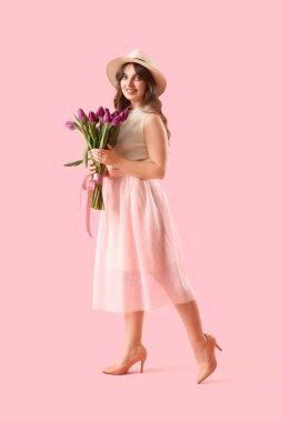 Pembe arka planda güzel mor lalelerle dolu buketi olan güzel genç bir kadın.