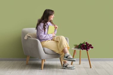 Yeşil duvarın yanında güzel mor lalelerle dolu kitap ve masa okuyan güzel bir kadın.