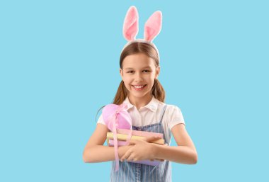 Paskalya tavşanı kulakları, yumurtası ve mavi arka planı olan sevimli küçük bir kız.