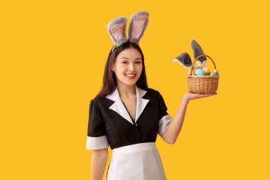 Sarı arka planda Paskalya yumurtaları olan tavşan kulaklı genç Asyalı oda hizmetçisi.