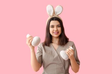 Pembe arka planda bitki torbalarıyla tavşan kulaklı kadın masaj terapisti. Paskalya kutlaması