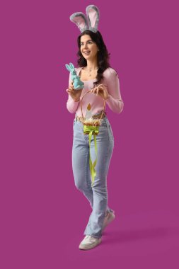 Tavşan kulaklı güzel bir kadın. Paskalya tavşanı ve mor arka planda yumurtalar.