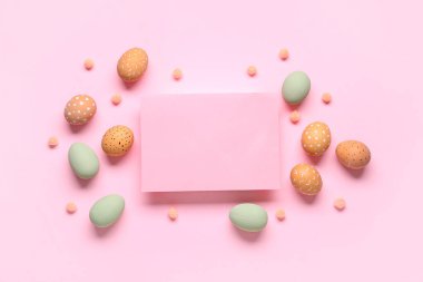 Paskalya yumurtaları ve pembe arka planda boş bir kart. Üst görünüm