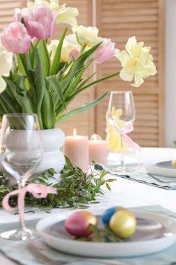 Çiçek, çatal bıçak, mum ve boyalı yumurta dolu Paskalya sofrası.