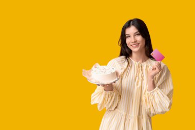 Sarı arka planda tatlı bento keki ve kredi kartı olan güzel genç bir kadın. Uluslararası Kadınlar Günü