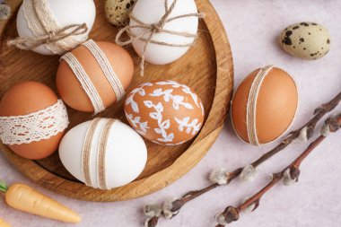 Wooden plate with decorated Easter eggs, gift boxes and willow branches on white background clipart