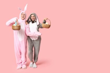 Pembe arka planda Paskalya sepetleri olan tavşan kostümlü güzel bir çift.