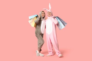 Pembe arka planda alışveriş torbaları olan tavşan kostümlü güzel bir çift. Paskalya kutlaması