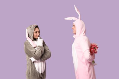 Mor arka planda bir buket lale olan tavşan kostümlü güzel bir çift. Paskalya kutlaması