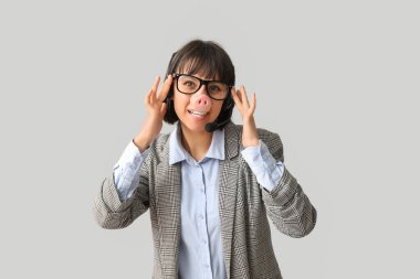 Kulaklık ve domuz burnu takan, gri arka planda gözlük takan komik, genç bayan teknik destek işçisi. Aptal günü.