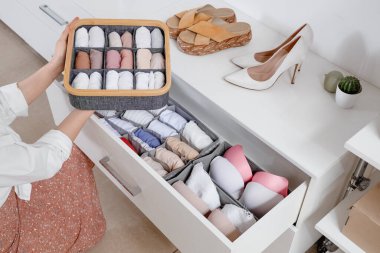 Dolaptaki organizatörlerde temiz giysileri olan güzel genç bir kadın, yakın plan.