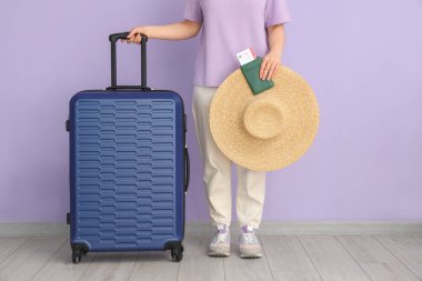 Bavulu, şapkası, pasaportu ve leylak arka planda bileti olan genç bir kadın.