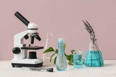 Laboratuvar cam ve mikroskobu, pembe duvarın yanındaki beyaz masada doğal kozmetik ürünlerini hazırlamak için.