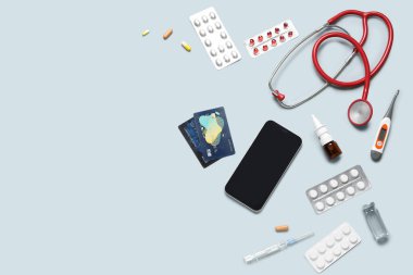 Gri arka planda modern cep telefonu, kredi kartı, farklı ilaçlar ve steteskop kompozisyonu
