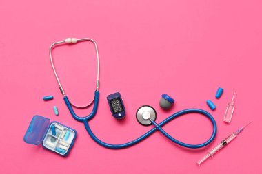 Composition with pulse oximeter, syringe, stethoscope and pill box on pink background clipart