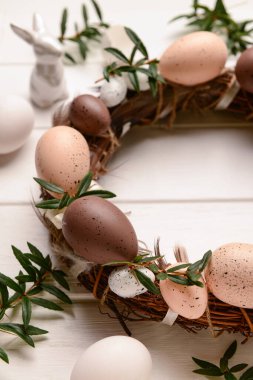 Beyaz ahşap masa üzerinde yumurta ve çiçeklerle süslenmiş Paskalya çelengi.