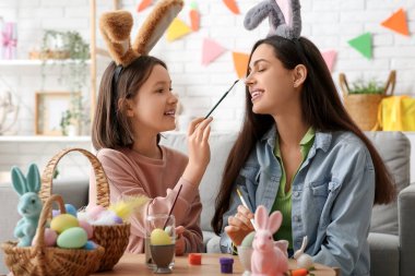 Küçük kız ve annesi tavşan kulaklı. Oturma odasında paskalya yumurtası boyuyorlar.