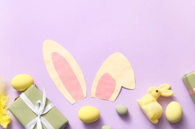 Paskalya yumurtaları ve leylak arkaplanda hediye kutuları olan kağıt tavşan kulakları.