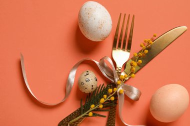 Turuncu arka planda Paskalya yumurtası ve mimoza çiçekli sofra takımı.