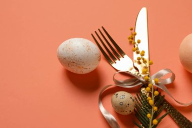 Turuncu arka planda Paskalya yumurtası ve mimoza çiçekli sofra takımı.