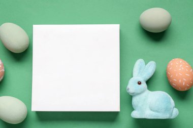Boyalı yumurtalar, Paskalya tavşanı ve yeşil arka planda boş bir kart. Yakın çekim.