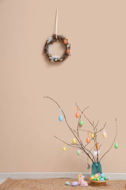 Bej duvarın yanındaki vazoda Paskalya yumurtaları olan dallar.