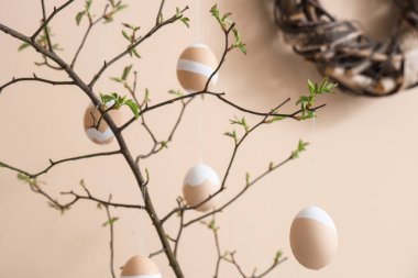 Bej duvarın yanında Paskalya yumurtaları olan ağaç dalları, yakın plan.