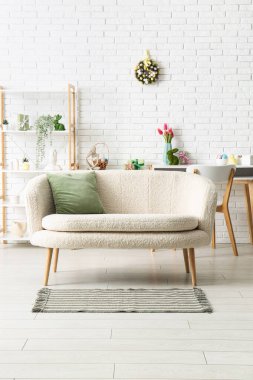 Kanepe, raf ve Paskalya çelengi oturma odasındaki beyaz tuğla duvara yumurtalarla süslenmiş.