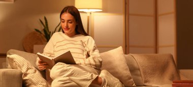 Genç bir kadın akşamları kanepede kitap okuyor.