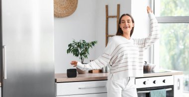 Mutfaktaki masada oturan, kablosuz hoparlörlü mutlu kadın.