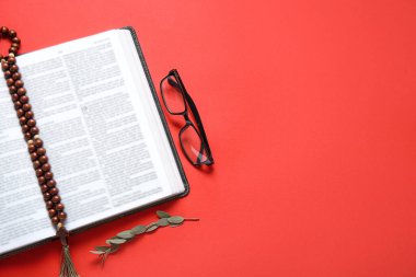 Kırmızı arka planda kutsal kitabı, gözlüğü ve tespihi aç.