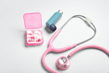 Astım spreyi, steteskop ve gri arka planda bir kutu hap.