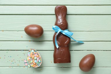 Çikolatalı Paskalya yumurtaları, yeşil ahşap arka planda serpiştirilmiş tavşanlar.
