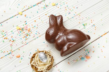 Çelenkli çikolatalı tavşan ve beyaz ahşap arka planda folyoda paskalya yumurtası.