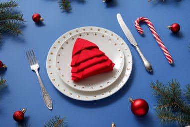 Mavi arka planda katlanmış peçete ve Noel süslemeleri ile şölen masası ayarları, yakın plan